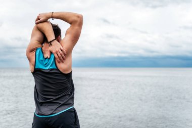 Sahilde spor kıyafetleri giyen tanınmamış bir adam idmandan sonra esniyor..