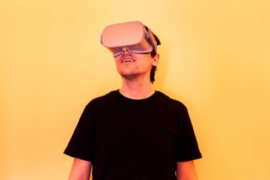 Sanal gerçeklik gözlüğü takan oyuncu evde sarı arka planda eğleniyor..