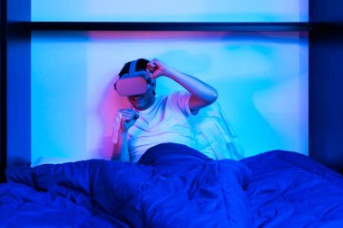 Oyuncu çocuk sanal gerçeklik gözlüğü kullanıyor. Yatağında eğleniyor..