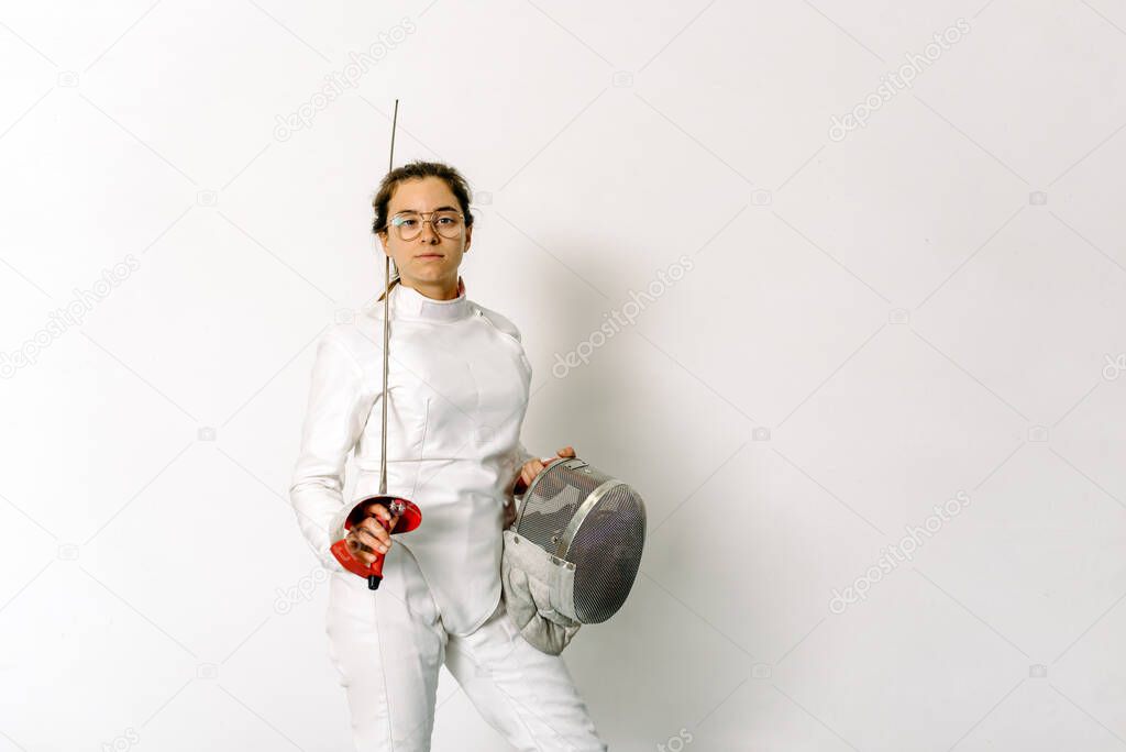 Expressive girl wearing fencing suit and holding rapier looking at camera against white background.