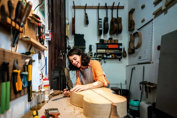 Gitar yaparken gülümseyen ve geleneksel atölyede çalışan genç bir kadın..