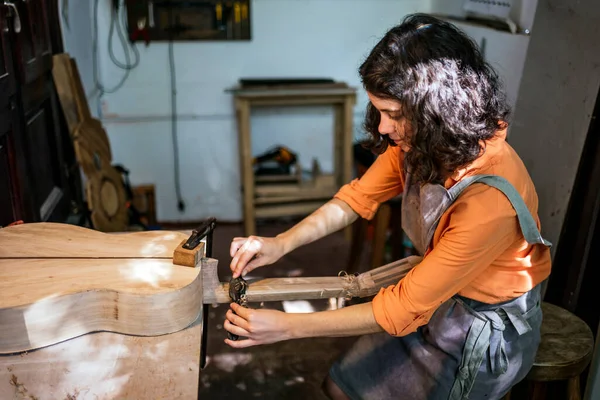 Kadın Luthier müzik aleti atölyesinde gitar çalıyor.