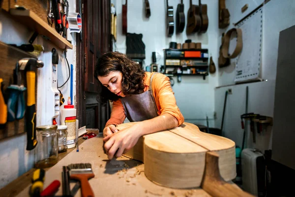 Kadın Luthier müzik aleti atölyesinde gitar çalıyor.