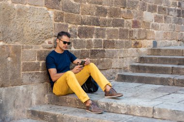 Cep telefonlu genç latin adam dışarıda oturuyor.