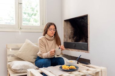 Evde kahvaltı yaparken cep telefonu kullanan genç Latin kadın..