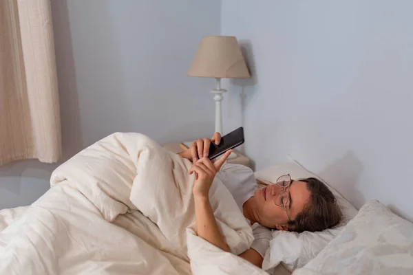 Młoda Latynoska z telefonem komórkowym leżąca w łóżku — Zdjęcie stockowe