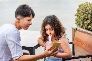 Anne ve kızı milkshake içip cep telefonuna bakıyorlar.