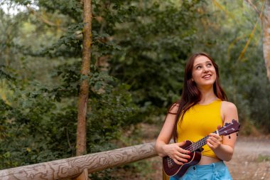 Genç beyaz kadın parkta ukelele oynuyor.