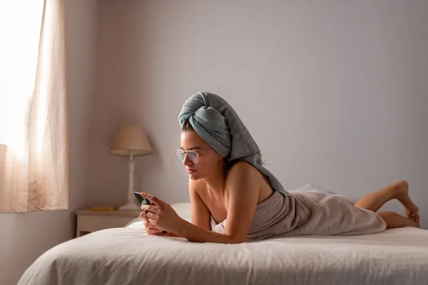 Młoda Latynoska świeżo kąpana z telefonem komórkowym w łóżku — Zdjęcie stockowe