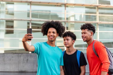 Bir grup afro Latin erkek arkadaş şehirde cep telefonuyla selfie çekip eğleniyorlar..