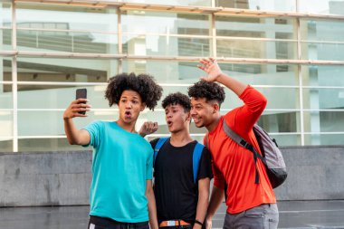 Bir grup afro Latin erkek arkadaş şehirde cep telefonuyla selfie çekip eğleniyorlar..