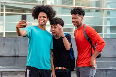 Bir grup afro Latin erkek arkadaş şehirde cep telefonuyla selfie çekip eğleniyorlar..