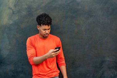 Duvara karşı cep telefonu kullanan Afro Latin bir genç.