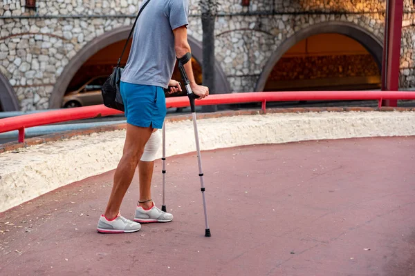 Unrecognizable young man with crutches walking in the city