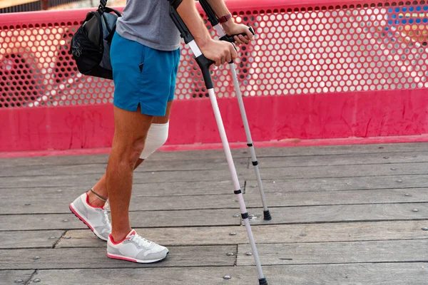 Unrecognizable young man with crutches walking in the city