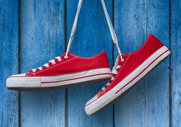 Κόκκινο πάνινα παπούτσια που κρέμονται σε μπλε φόντο ξύλινη — Φωτογραφία Αρχείου