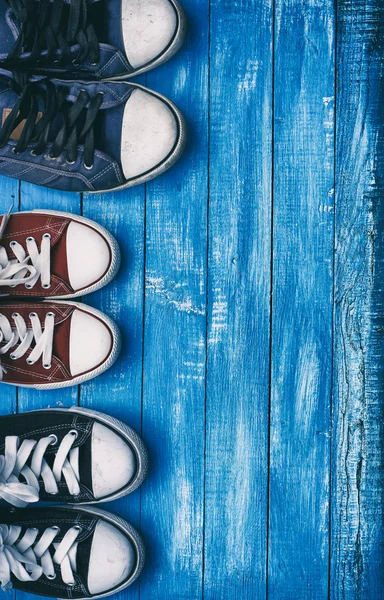 Три пари старих кросівок на синьому дерев'яному фоні — стокове фото