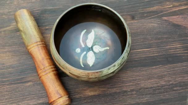 Cuenco para cantar con agua y un palo de madera sobre la mesa — Vídeos de Stock