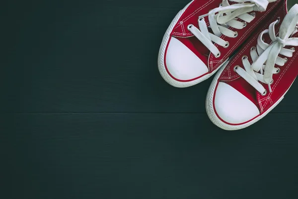 Paio di scarpe da ginnastica rosse giovani su uno sfondo di legno nero — Foto Stock