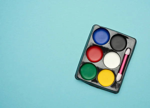 palette with multi-colored makeup paints on a blue background, copy space