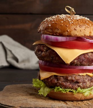 Domatesli duble çizburger, soğan, barbekü pirzolası ve eski bir tahta kesme tahtasında susamlı ekmek. Fast food, yakın çekim.