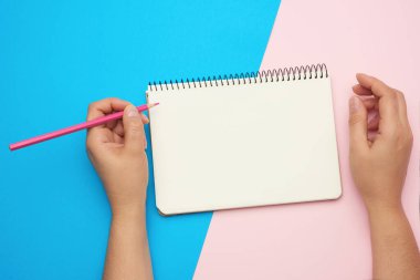 Mavi arka planda temiz çarşafları olan açık not defterini tutan iki kadın el.