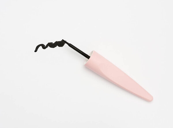 sample of black eyeliner and plastic brush on white background