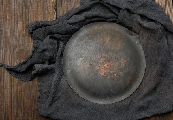 metallic round plate  and black kitchen textile towel folded on a brown wooden table, top view, empty space
