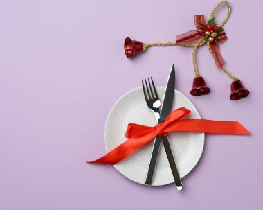 yuvarlak beyaz seramik tabak, mor bir zemin üzerinde bıçak ve çatal, noel ve yeni yıl için şenlik sofrası, üst görünüm