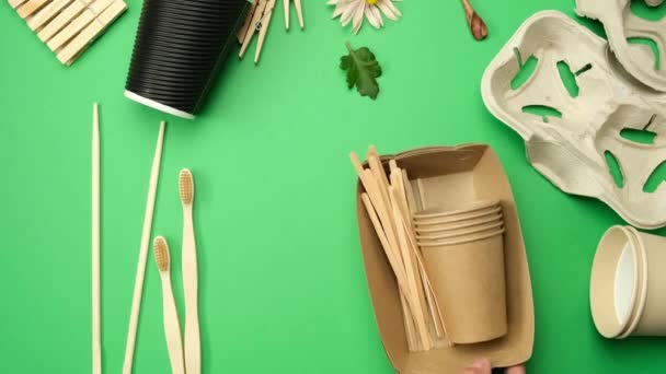 リサイクル可能な素材や使い捨ての紙コップ 緑の背景の木のフォークで作られた様々なアイテムがトップビュー 廃棄物ゼロ — ストック動画