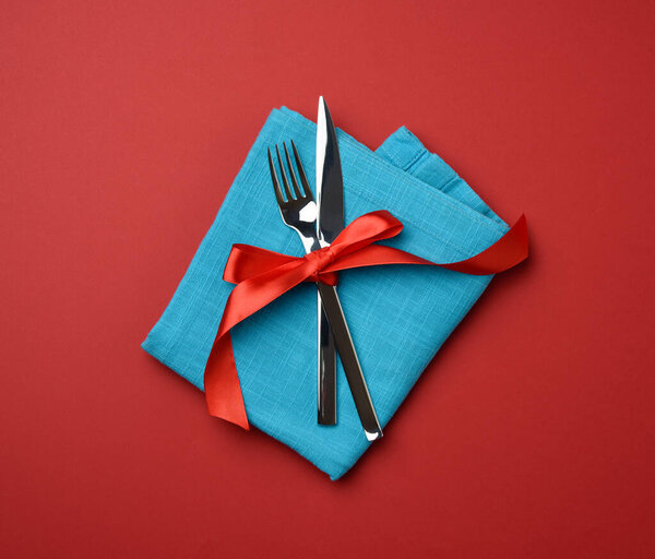 металлическая вилка и нож связаны красной шелковой лентой, красный фон, вид сверху