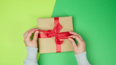 Kadın elleri hediye kutusunda kırmızı ipek kurdeleyi çözer, yeşil arka plan, üst manzara