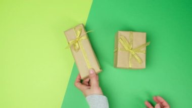 İki kadın eli yeşil bir yüzeye koyuyor altın kurdeleyle bağlanmış bir kutu, üst manzara.