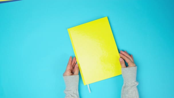 2人の女性の手が青い背景に白いシートの黄色いノートブックのページをめくり — ストック動画
