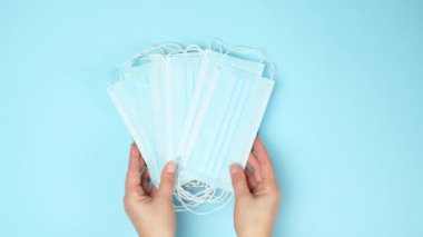 Mavi arka planda boş seramik tabak. Kadın elleri tek kullanımlık tıbbi maskeyi üste koyar, restoran kapatma konsepti, üst görünüm..