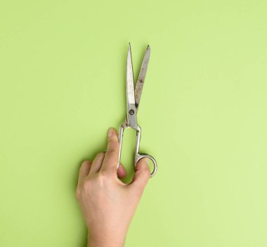 El, yeşil arka planda metal makas tutuyor.