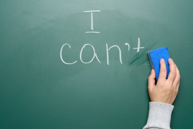 Kadın eli, tebeşir yeşili tahtayı silmek için mavi bir sünger tutuyor ve cümlenin bir kısmını siliyor, motivasyon ve kendine güven.