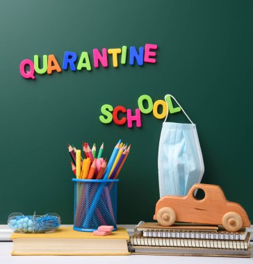 Yeşil tebeşir tahtasında asılı çok renkli plastik bir mektup karantinası, tek kullanımlık tıbbi maske.