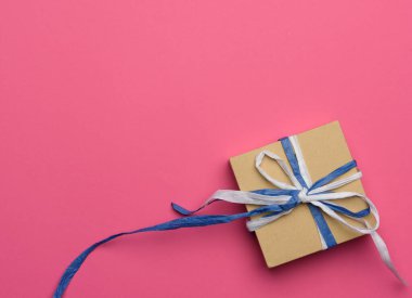 Kahverengi kraft kağıdına sarılı bir hediye. Pembe arka plan, üst manzara.
