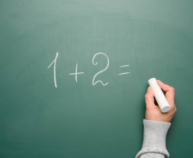 Yeşil tebeşirle beyaz tebeşirle yazılmış matematik örneği ve beyaz tebeşirli bir kadın eli, bir artı iki.