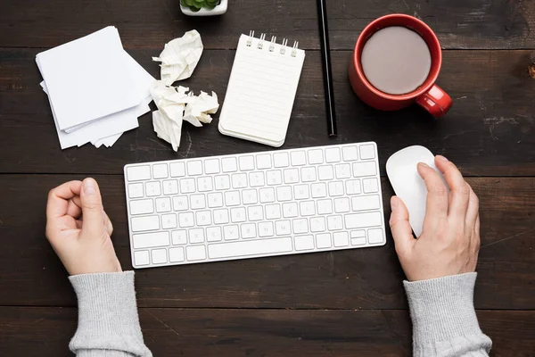 white wireless keyboard and mouse on a wooden brown table, next to a white cup with coffee, top view