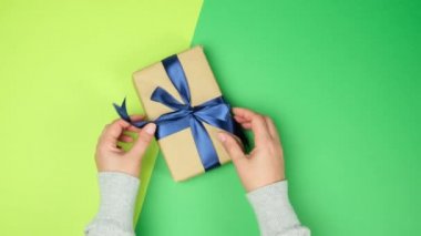 Kadın eli yeşil yüzeye sarılıp mavi kurdeleli hediyeler takar, üst manzara, şenlikli arka plan