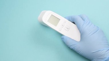 Mavi lateks eldivenler, sıcaklığı ölçmek için bir elektronik termometre tutar. Temassız bir cihaz.
