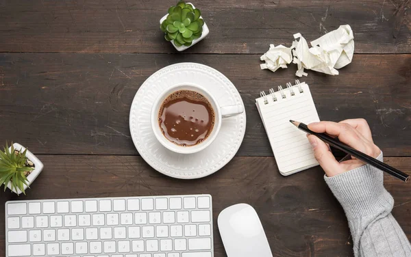 white wireless keyboard and mouse on a wooden brown table, next to a white cup with coffee, top view