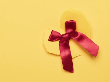 Sarı kağıt kalp ve sarı arka planda kırmızı ipek yay, düz yatıyordu.