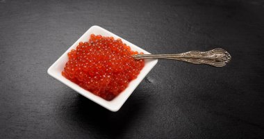 Taze tahıllı kırmızı somon balığı havyarı beyaz bir seramik kasede siyah bir taş zemin üzerinde, kapat