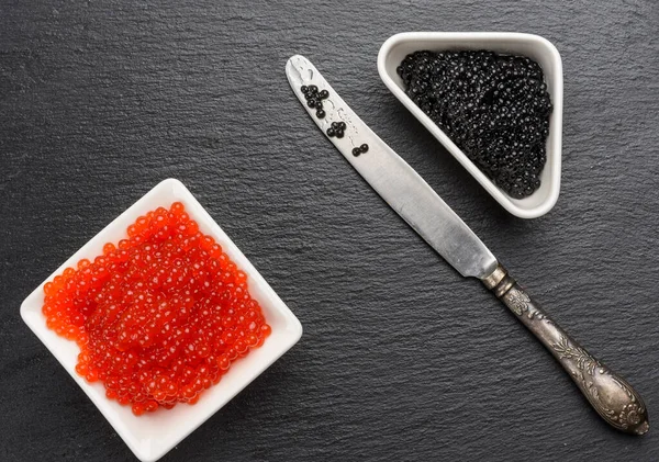 grainy caviar of paddlefish fish in a white ceramic plate and red chum salmon caviar in a white ceramic bowl,  black background, top view