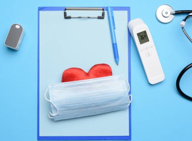 Maske ve nabız oksimetresi, elektronik termometre ve mavi arka planda diğer tıbbi malzemeler.