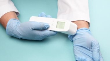 Mavi lateks eldivenler, sıcaklığı ölçmek için bir elektronik termometre tutar. Temassız bir cihaz.