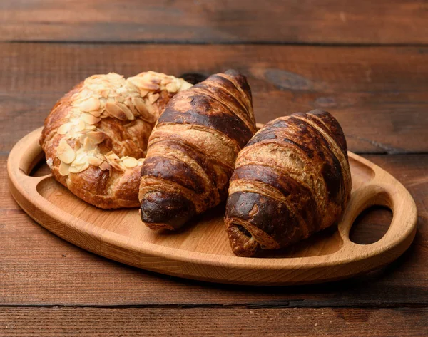 two baked croissants lie on a wooden tray, food on a brown background